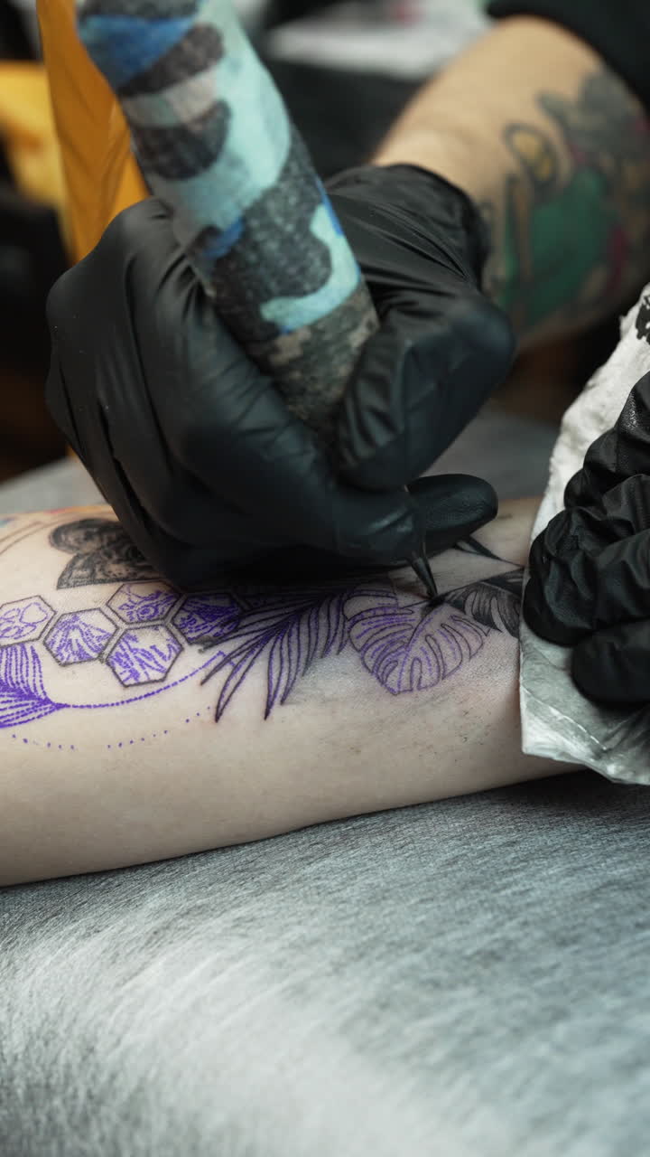 Vertical close up shot of tattoo artist tattooing a woman's forearm, interior
