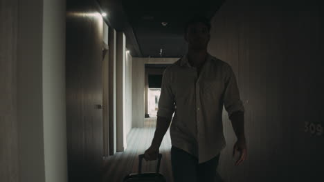 Confident-guy-with-luggage-going-along-corridor.-Man-opening-door-hotel-room.