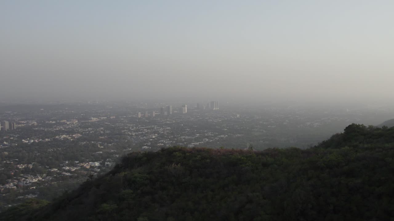 Distant view of Islamabad’s skyline emerging through haze from Margalla Hills during early evening. Islamabad