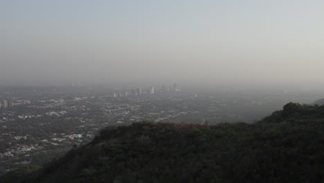distant view of islamabad’s skyline emerging through haze from margalla hills during early evening. islamabad