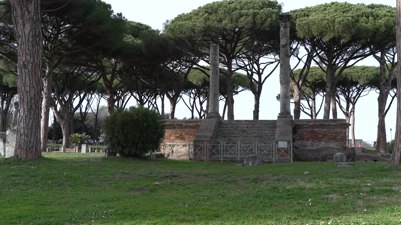 Piattaforma in mattoni simile a un tempio con pilastri alti situata in un campo erboso sotto pini marittimi in un sito storico romano