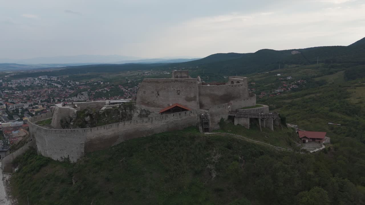 Ripresa aerea con drone che rivela la Fortezza di Deva arroccata sulla sua collina, circondata dallo spettacolare scenario rumeno