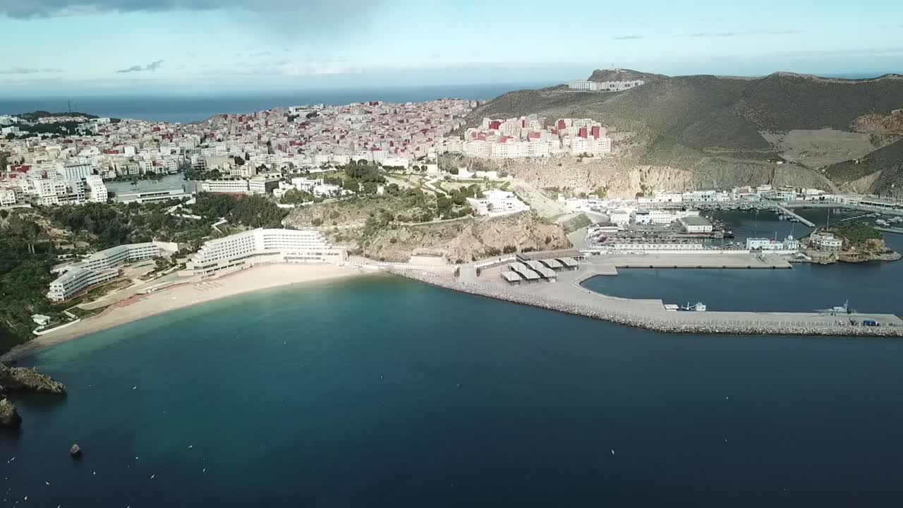 Stunning aerial drone shot showing a golden sandy beach embraced by the rugged terrain of the Rif Mountains in Al Hoceima, Morocco