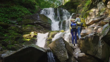 una joven pareja de turistas admira la cascada que se paran en un abrazo la vista trasera 4k 10 bit vid