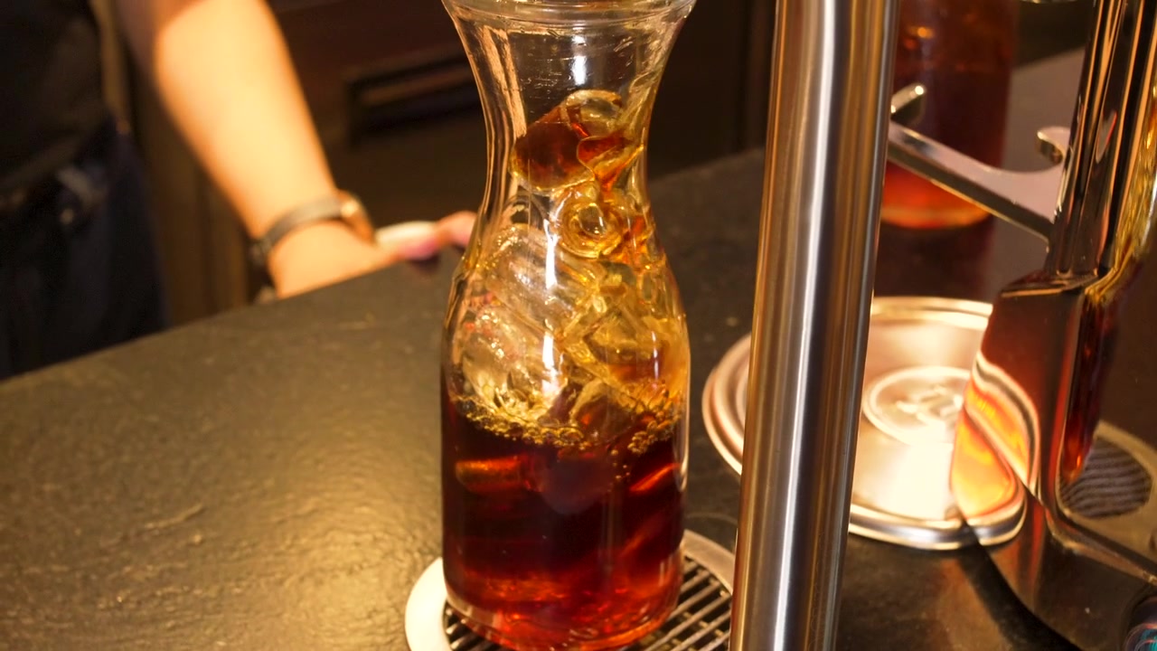 Barista che riempie una caraffa di vetro con caffè cold brew da un erogatore a rubinetto in acciaio inossidabile in un bar caffetteria specializzato