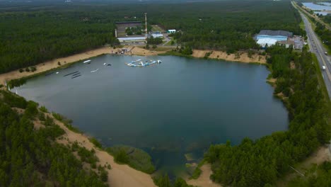 aerial drone revealing shot showing a large blue colored lake also a former sand quarry mining open pit during a cloudy day, with trees around and a bouncy inflatable castle attraction in the water