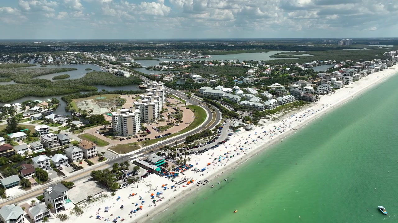 Inquadratura cinematografica a volo d'uccello della costa di Bonita Springs, che mostra il Golfo del Messico, grattacieli sulla spiaggia, case sul lungomare e rigogliosi canali che si snodano attraverso il quartiere.