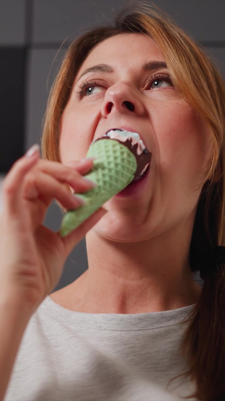 Close up of woman enjoying ice cream cone bringing it to her mouth and taking bites. focus remains on interaction between hand holding green waffle cone with chocolate coating and vanilla