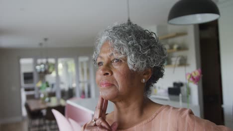 animation of thoughtful african american senior woman standing in kitchen