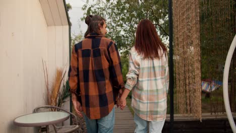 Shooting-from-behind:-A-red-haired-girl-with-her-long-haired-brunette-boyfriend-in-a-white-checkered-shirt-are-walking.-Rest-in-the-country-house