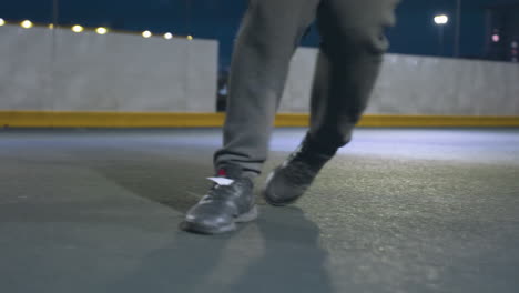 leg view of man in hoodie kicking soccer ball under bright streetlights on illuminated urban soccer field, featuring goal post and blurry cityscape in background