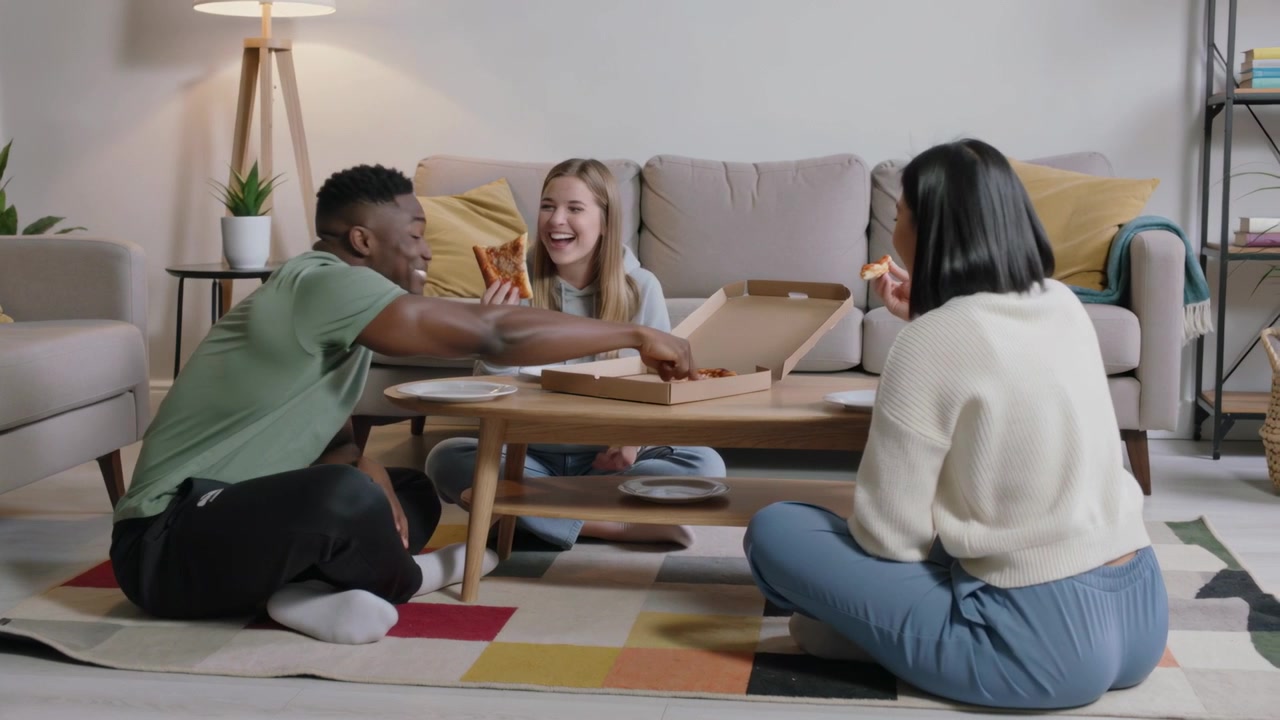 Venner deler pizzastykker og griner i stuen efter at have åbnet æsken og deler et måltid