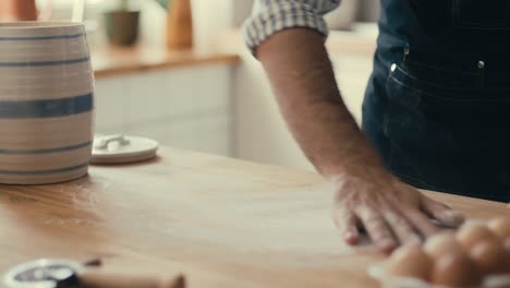 man dusting flour onto wooden kitchen table before baking