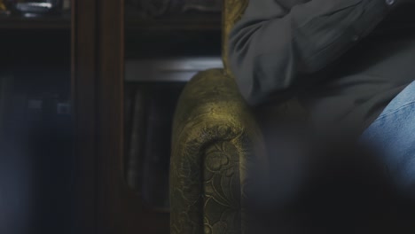 man sitting in armchair holding eye glasses with fidgeting fingers