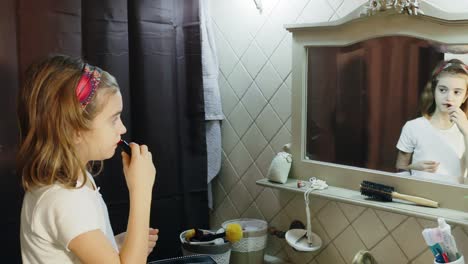 una niña linda intentando pintalabios en su cara por primera vez, mientras está en el baño frente al espejo