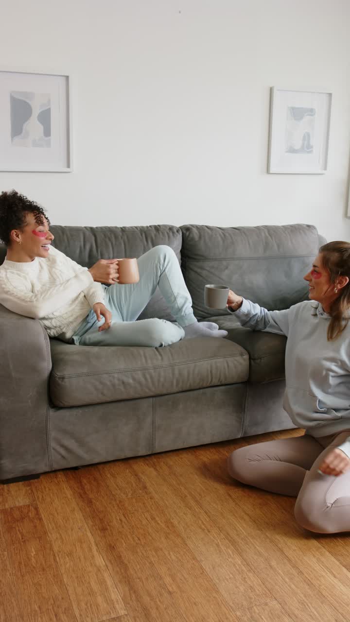 Vertical video: Diverse female friends exchanging smiles, clinking mugs at home for coffee toast