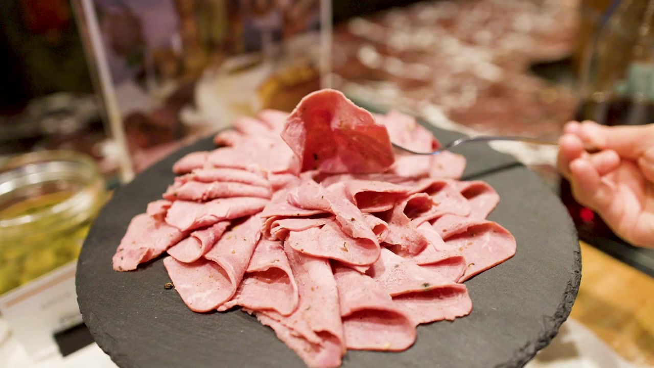 Una persona usa una forchetta per prendere fette di roast beef da un piatto di ardesia.