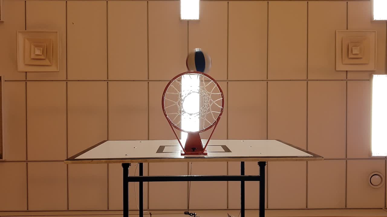 Indoor basketball hoop in gym at school. Two balls hitting the target net, low-angle perspective