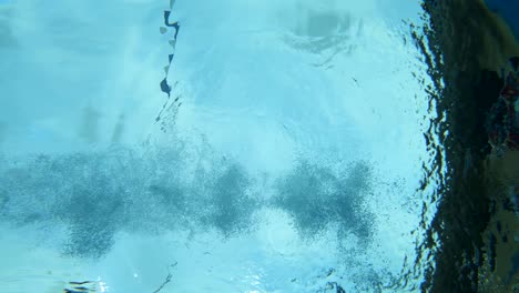 ángulo submarino de una mujer con traje de baño sumergiéndose en una piscina azul