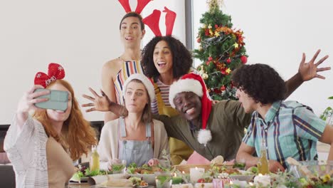 Feliz-Grupo-De-Amigos-Diversos-Sentados-A-La-Mesa-Y-Cenando-Juntos,-Tomándose-Selfie