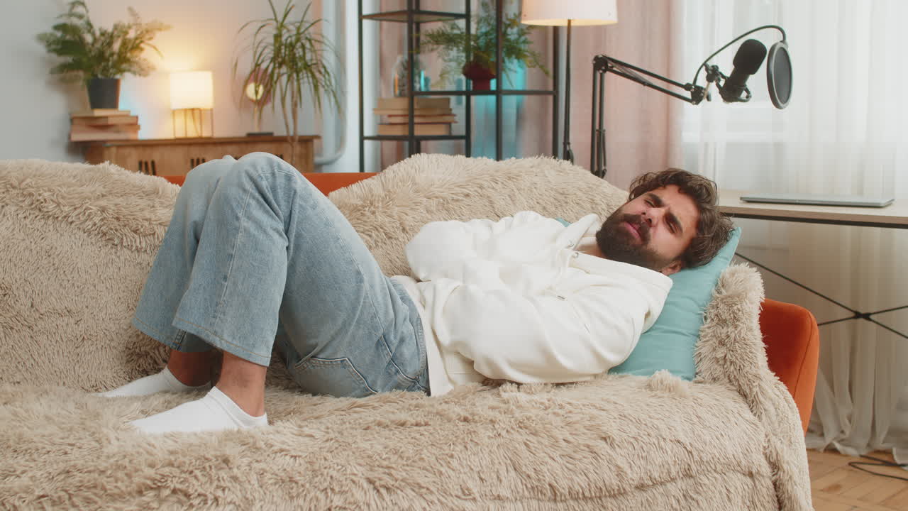 Young indian man lying on sofa feeling sudden strong abdominal stomach ache gastritis problem