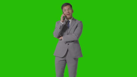 three quarter length studio shot of smiling businessman in suit talking on mobile phone against green screen 1