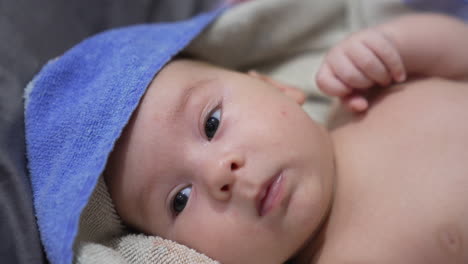 lovely bare child wrapped in towel lies on his back after washing. cute little baby waving tiny fist. close up.