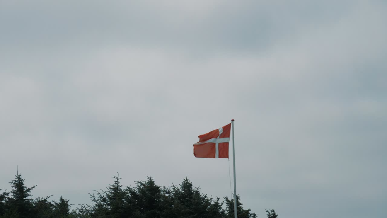Dansk flag blafrer i vinden med skyet himmelbaggrund i let slowmotion