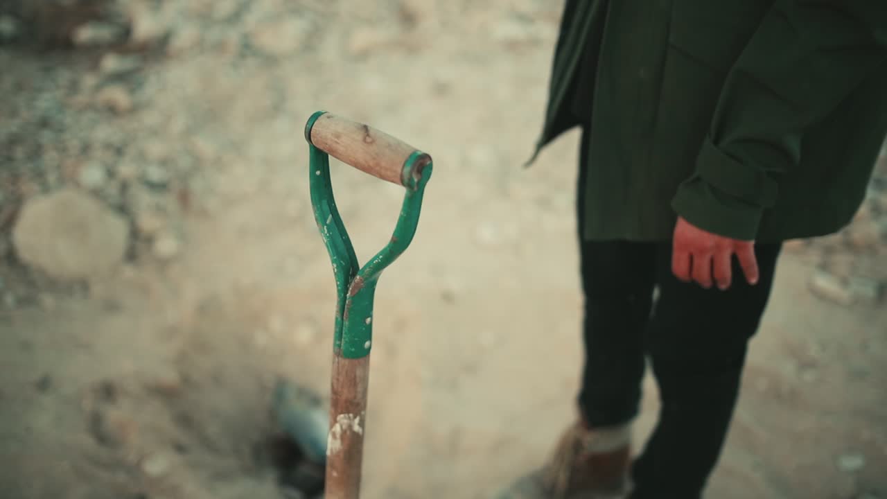 primer plano de un hombre que toma una pala para cavar en un entorno hostil y árido