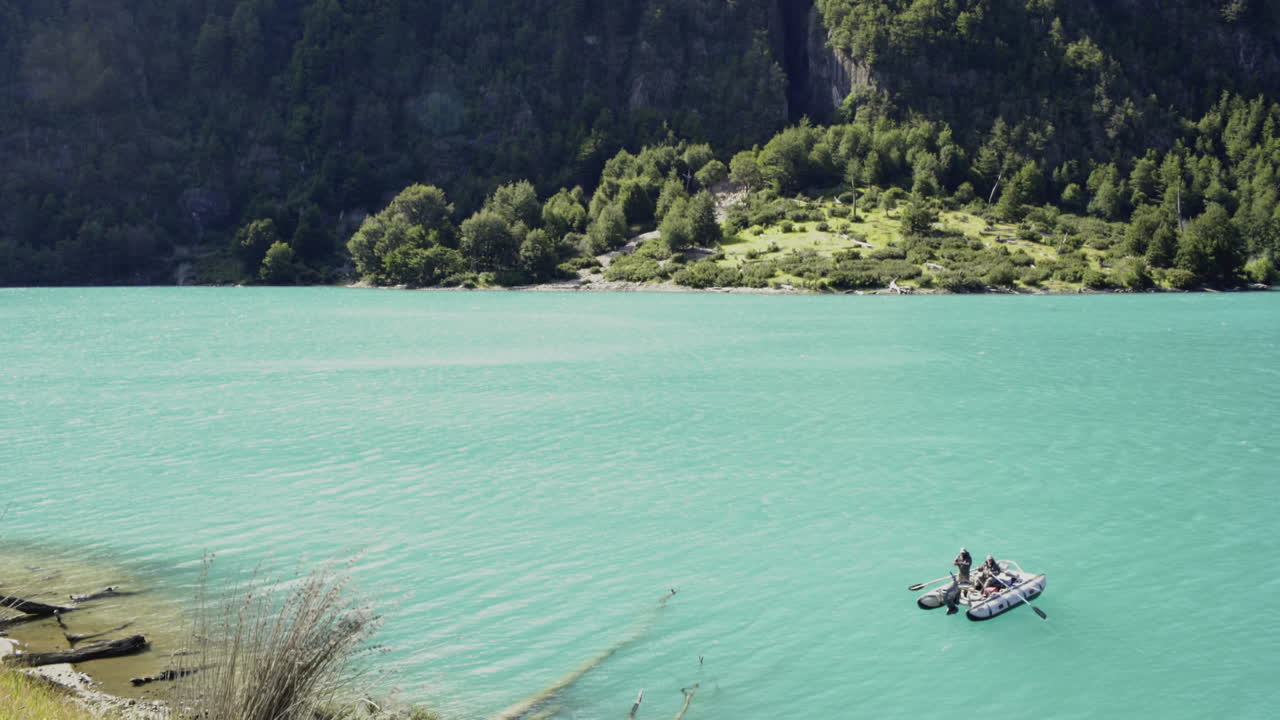 낮에 가파른 산이 보이는 청록색 호수에 떠 있는 배에서 두 명의 어부가 낚시를 하고 있다
