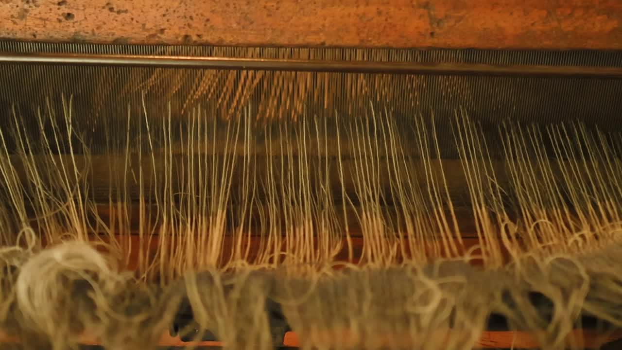 Detailed view of threads and mechanical parts of a weaving loom in motion.