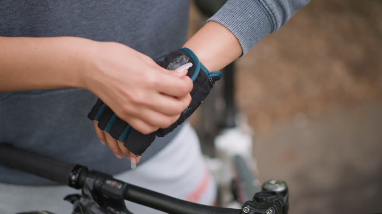 Woman Checking Glove Fit And Smoothing Palm On Handlebar, Closeup Of Hands And Helmet On Frame, Securing Strap And Positioning Grip, Calm PreRide Moment On Leafy Path With Focused Attention