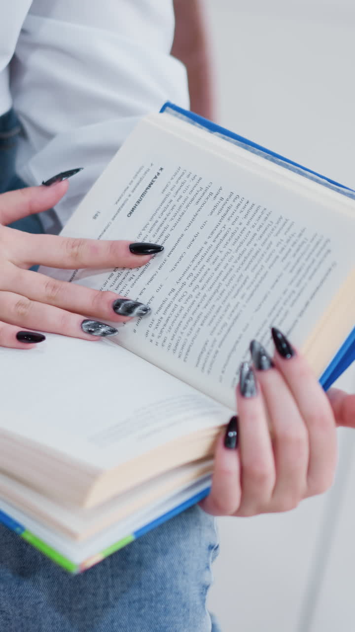 mujer con pantalones de jean con uñas pulidas negras sentada en un banco de madera hojeando páginas de un libro en un centro comercial brillante, los azulejos lisas reflejan la luz