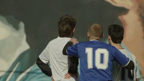 three football soccer players stand together, admiring a mural during a sunny day