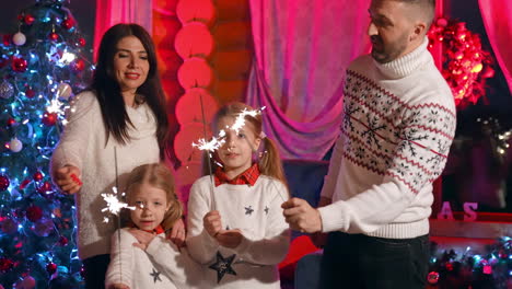 portrait of a happy family near christmas tree. young parents and little girls standing together and holding lights in new year night. christmas spirit.