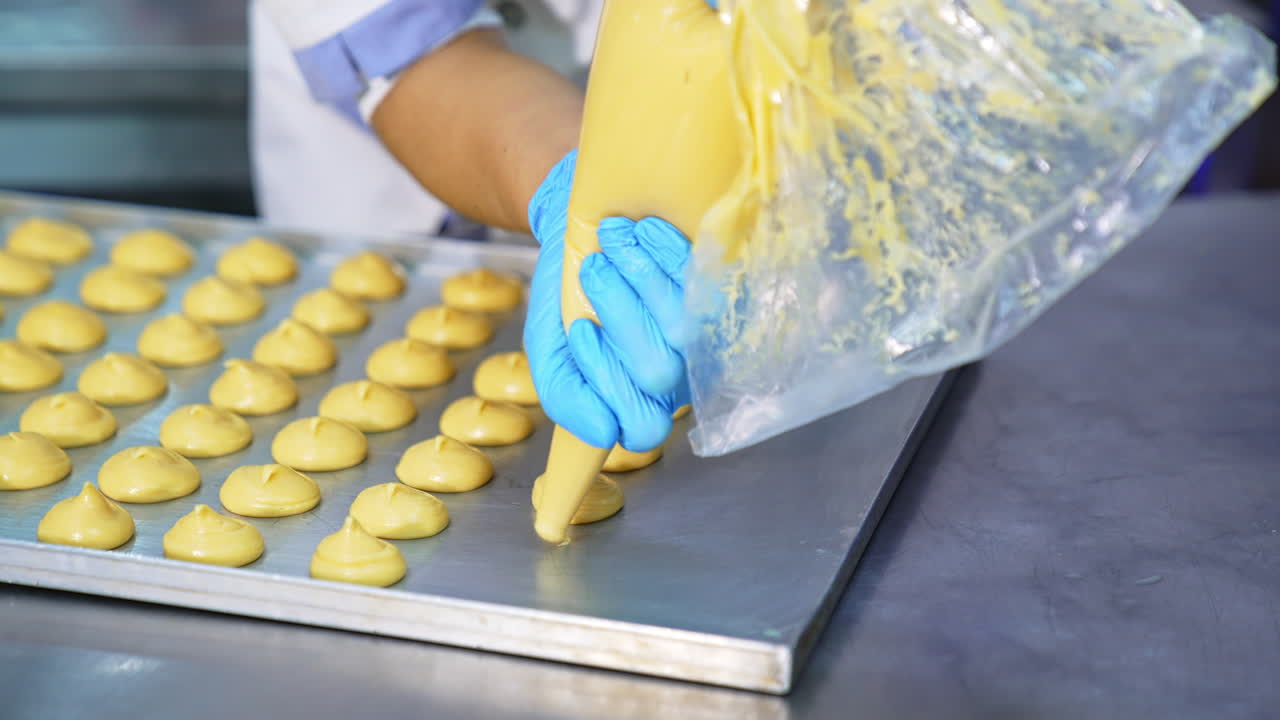 Confectioner squeezes choux pastry from a bag onto the baking sheet. Dough being prepared for baking in oven. Close up.