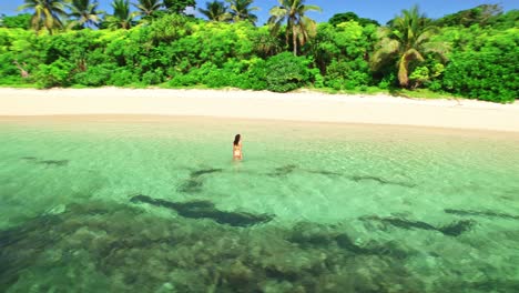 Happy-female-walking-through-turquoise-water-on-tropical-island-beachfront,-Yasawa,-Fiji