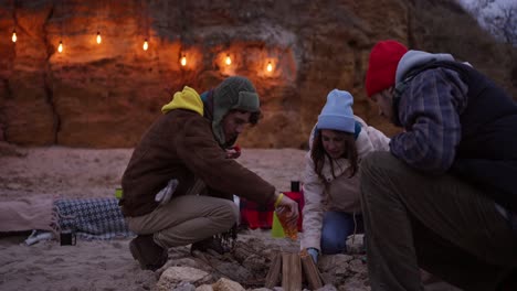 friends camping by a bonfire at the beach at sunset