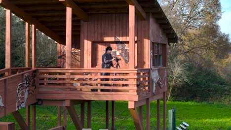 Fotógrafo-De-Viajes-Instalando-Una-Cámara-En-Un-Trípode-En-La-Terraza-De-Una-Casa-Forestal-De-Madera