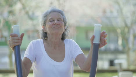 Happy-senior-woman-exercising-on-elliptical-trainer-in-park.