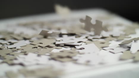 close up of white and gray puzzle pieces falling in slow motion on a white surface on a pile of pieces with a dark background. shot in 4k with shallow depth of field. smooth pan movement