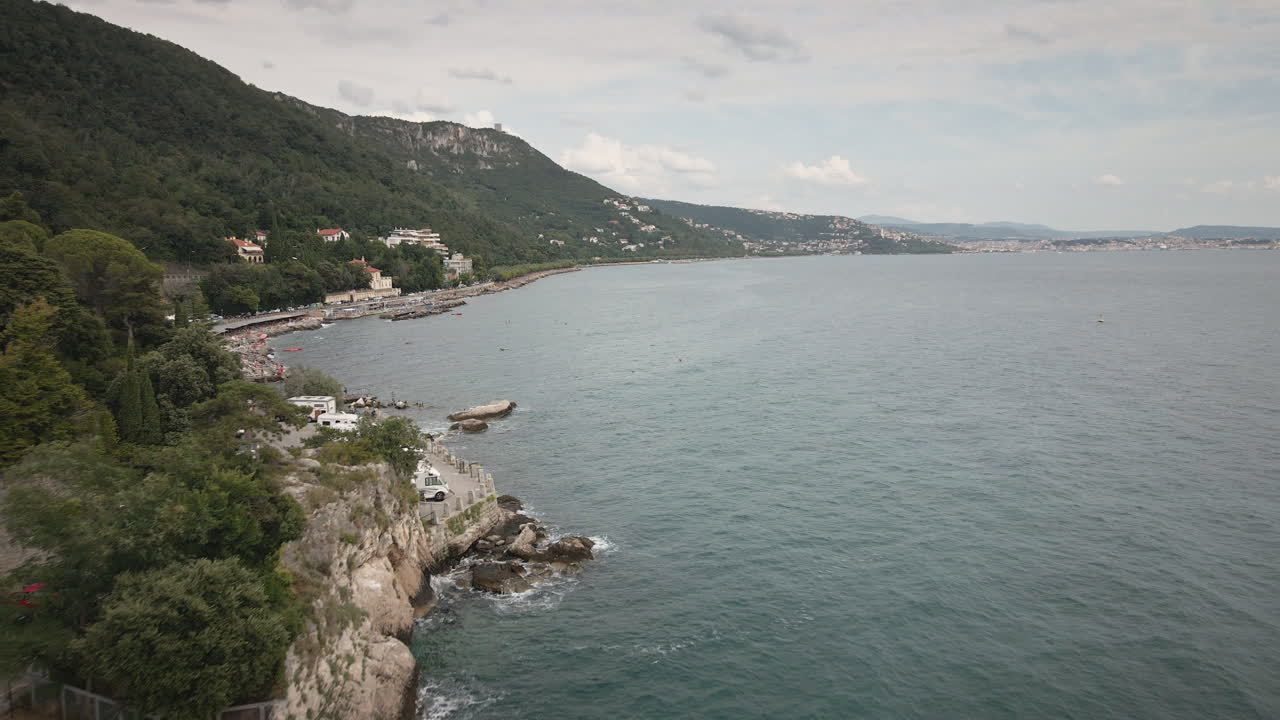 Un drone 4K UHD scorre fluidamente in avanti lungo la costa di Trieste sul Golfo di Trieste, Mare Adriatico, con scogliera, spiaggia e strada costiera — ideale per spot pubblicitari di viaggio, introduzioni.