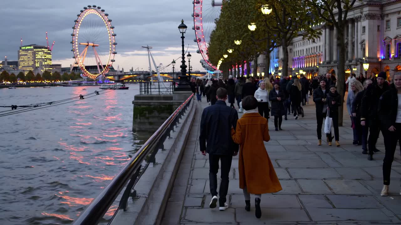 Evening cityscape video shot from a street-level angle, capturing a couple walking along a riverside