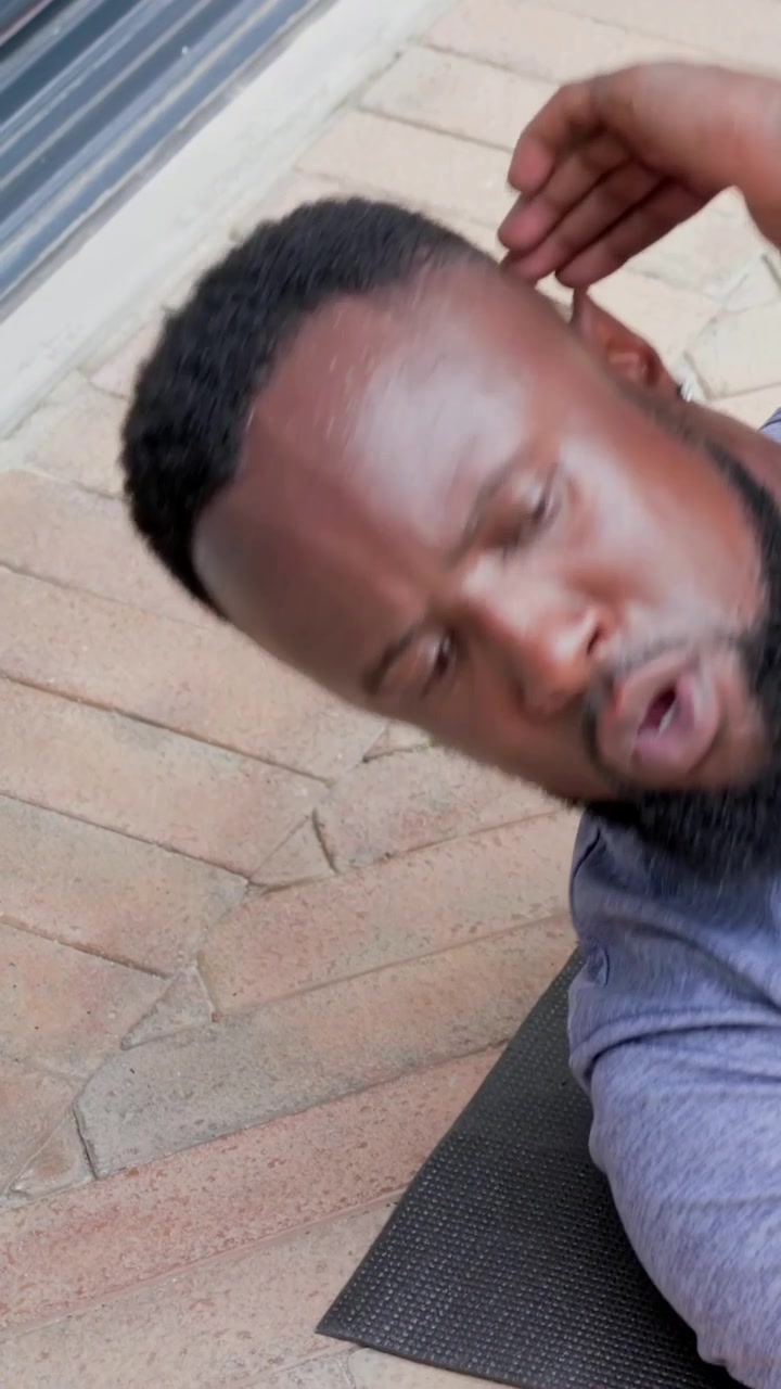 Vertical video: Gasping man in heather tee recovering post-workout, touching ear on patio mat