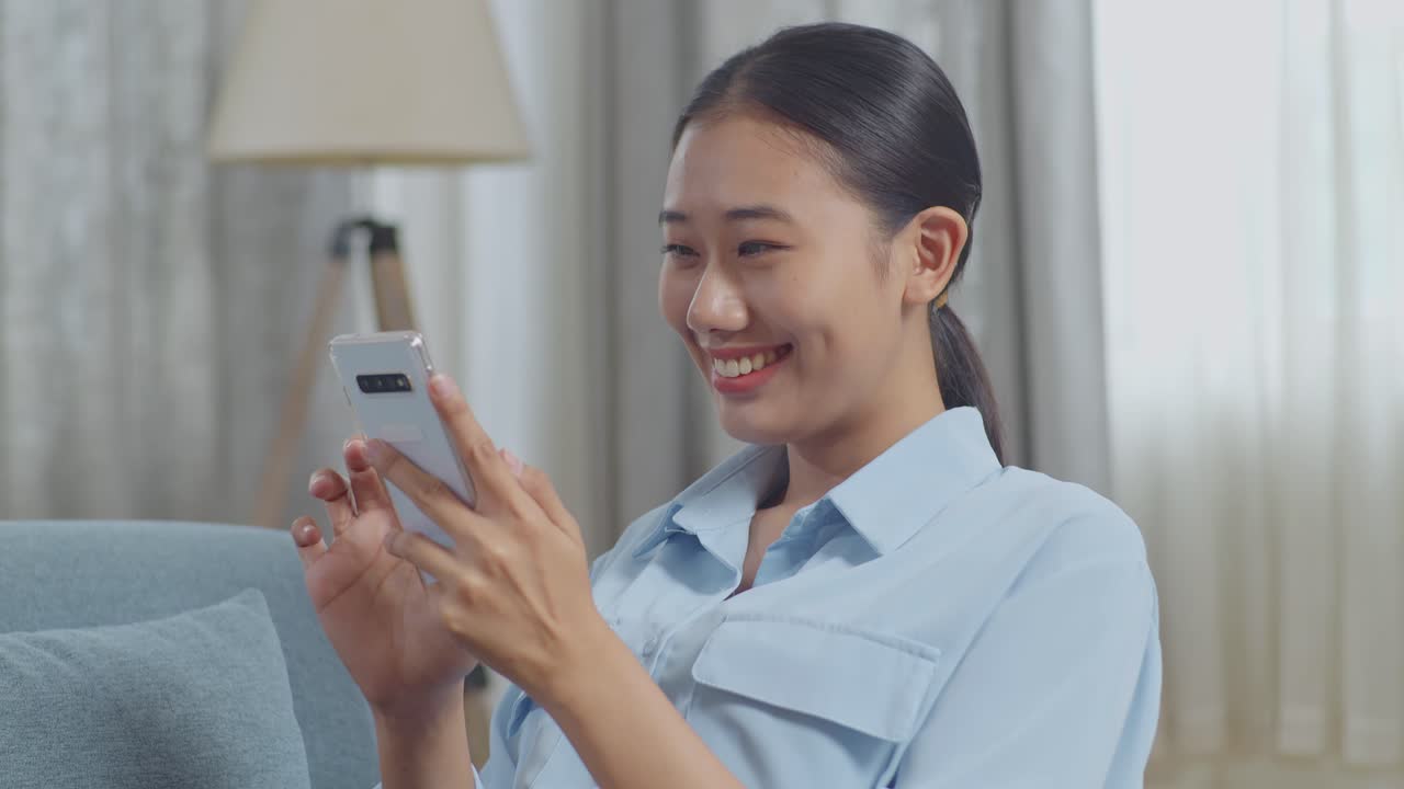 아시아 여성이 거실의 소파에 누워서 스마트폰을 사용하는 것을 즐긴다.
