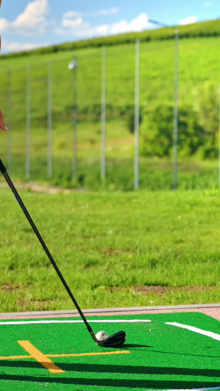 Close up of a golf club hitting a golf ball into a hole. Vertical