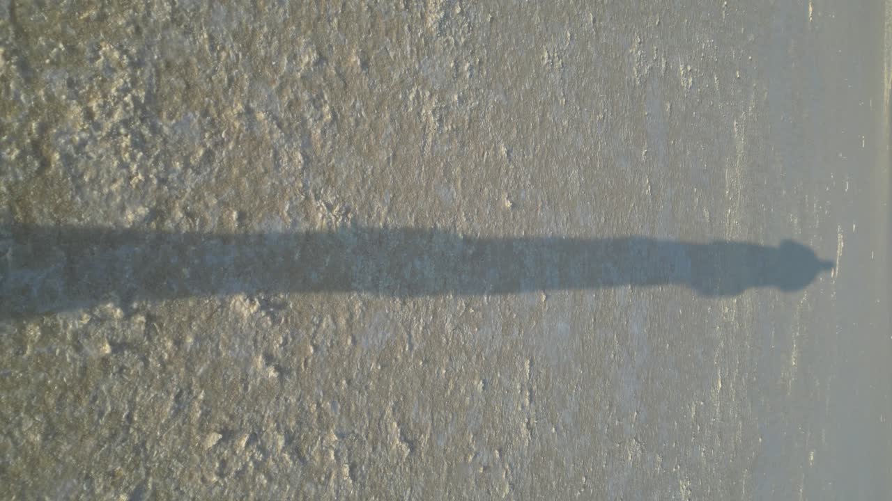 silueta de una persona caminando sobre un lago salado proyectada en el suelo durante la puesta del sol