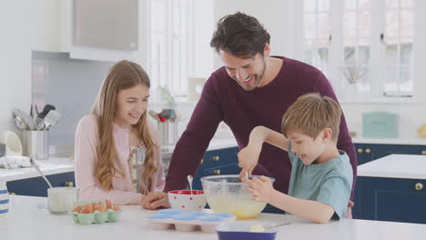 father with two children in kitchen at home having fun baking cakes together