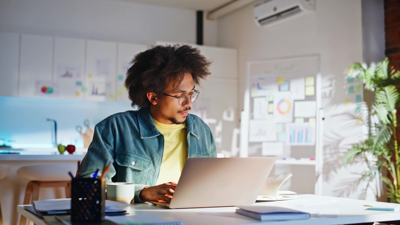 Startup founder typing laptop home office. Mixed race entrepreneur taking notes.