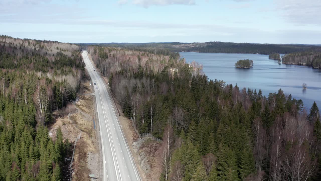 Drone shot of Swedish highway running through forest, cars driving by with lake in background